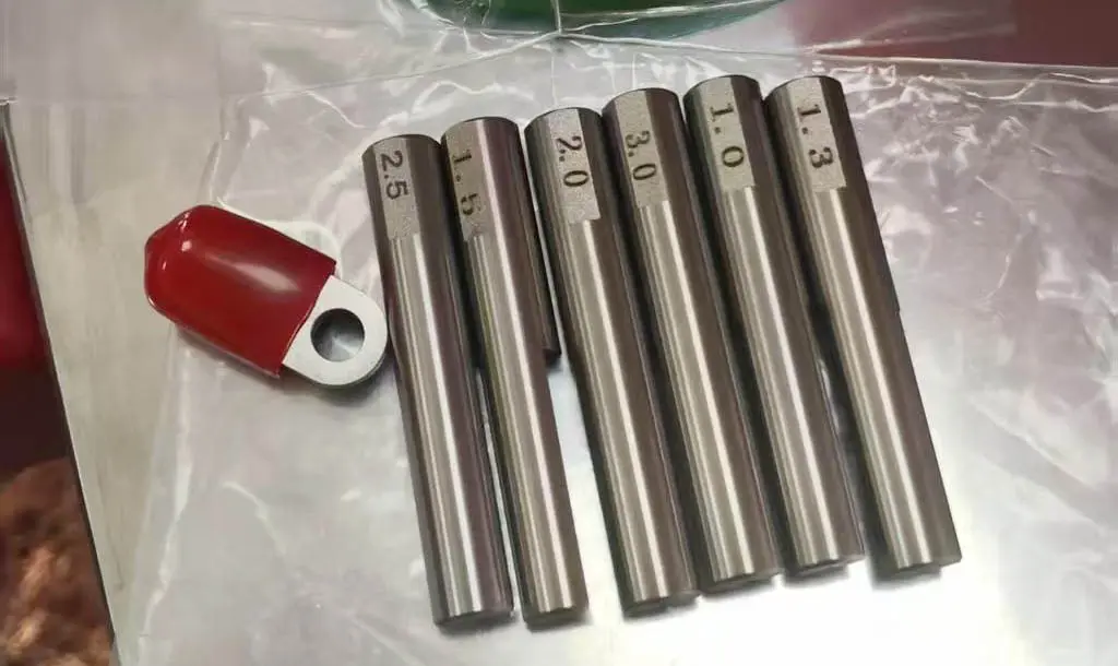 Bộ sáu mẫu dây hoặc ống kim loại chính xác với đường kính được ghi nhãn từ 1.0mm đến 2.5mm, được trưng bày trên một tấm nhựa với dụng cụ màu đỏ