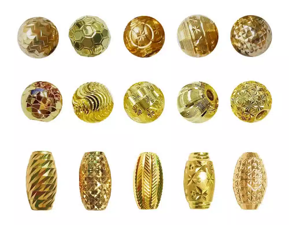 A display of assorted gold-toned beads in round and barrel shapes, featuring a variety of intricate surface textures and patterns including diamond facets, honeycomb, star motifs, wave engravings, and geometric cuts, arranged on a plain white background