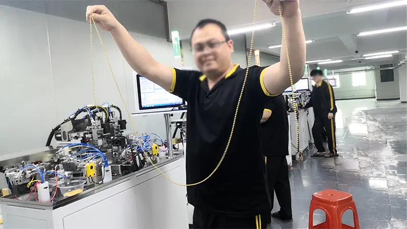 Một bàn tay đang cầm chiếc dây chuyền hạt tròn bằng vàng tinh xảo, các hạt vàng nhỏ đều đặn xâu chuỗi lại với nhau, lấp lánh ánh kim dưới ánh sáng.