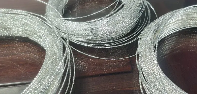 Những cuộn dây bạc dùng trong chế tác trang sức với bề mặt được cắt kim cương được sắp xếp trên bề mặt gỗ, thể hiện kết quả cắt chính xác