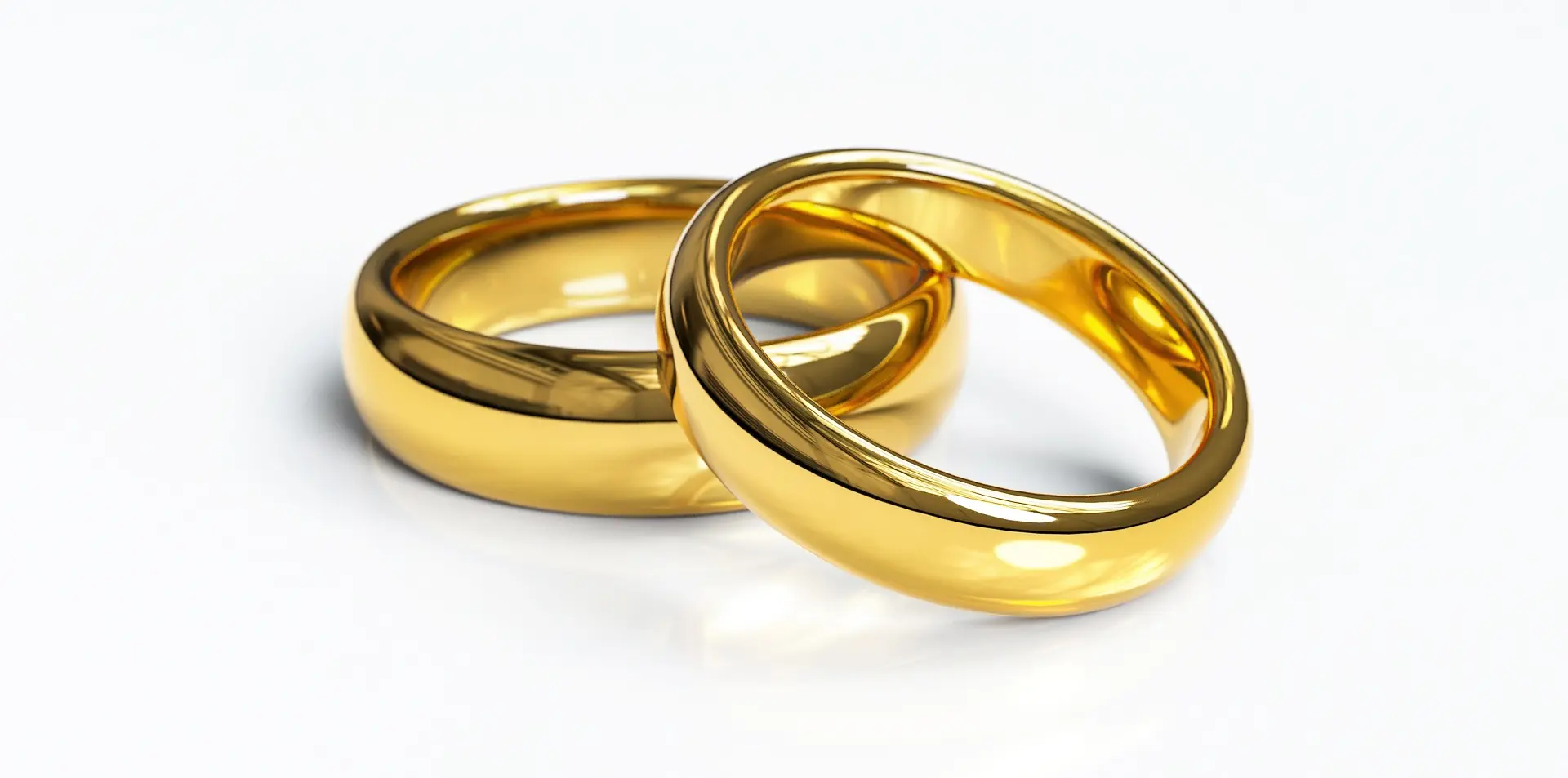 Two classic polished gold wedding bands with a smooth mirror finish, interlocked and resting on a clean white background, symbolizing marriage and eternal commitment.