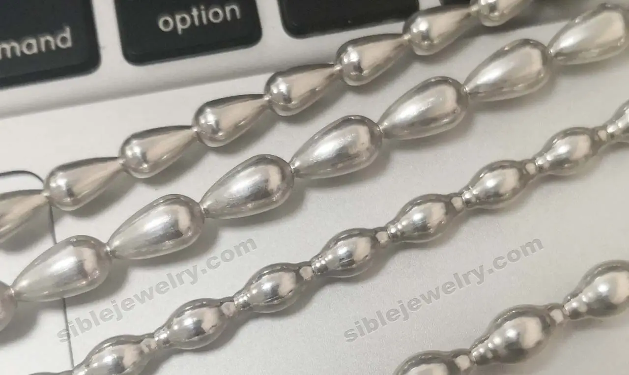 Chuỗi hạt kim loại bạc sáng bóng hình giọt nước được sắp xếp trên bề mặt trắng